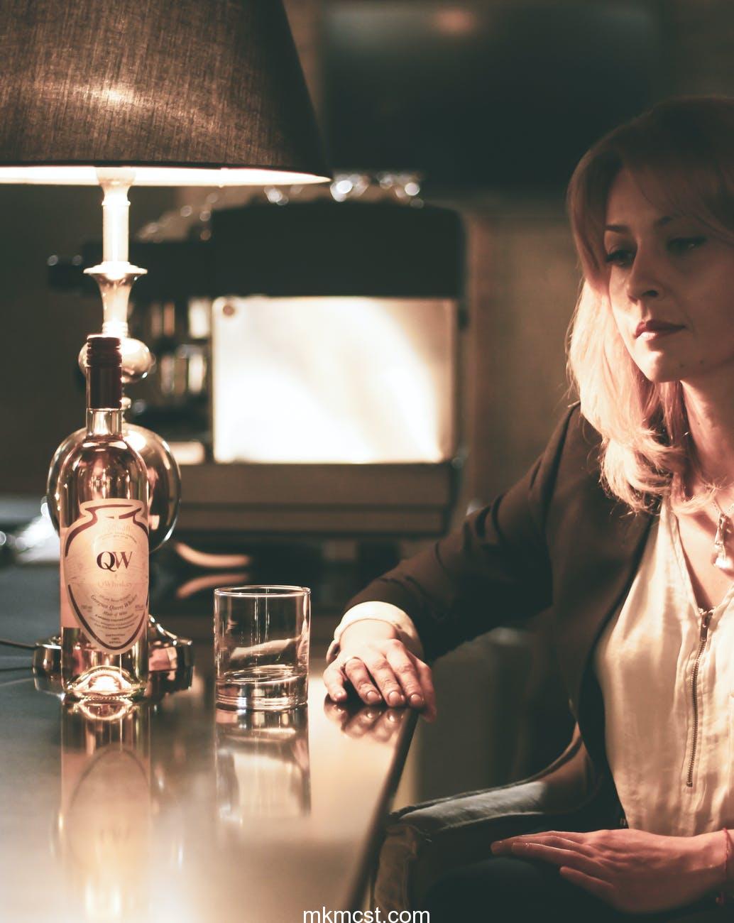 pensive young woman drinking alcohol beverage in bar